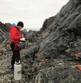 A person stands between a rock formation, wearing a red jacket.